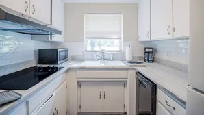 A compact kitchen with white cabinets, a black stove, a microwave, a sink, and a window with blinds. - Comfort Living Near LRMC, Medical Row
 (Lakeland)