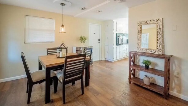 A dining area with a wooden table and chairs, a hanging light fixture, and a wooden console table with a mirror and decorative items. - Comfort Living Near LRMC, Medical Row
 (Lakeland)
