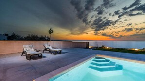 An outdoor pool area with lounge chairs and a view of the sunset over the ocean. - Cozy home in Privlaka (Privlaka)