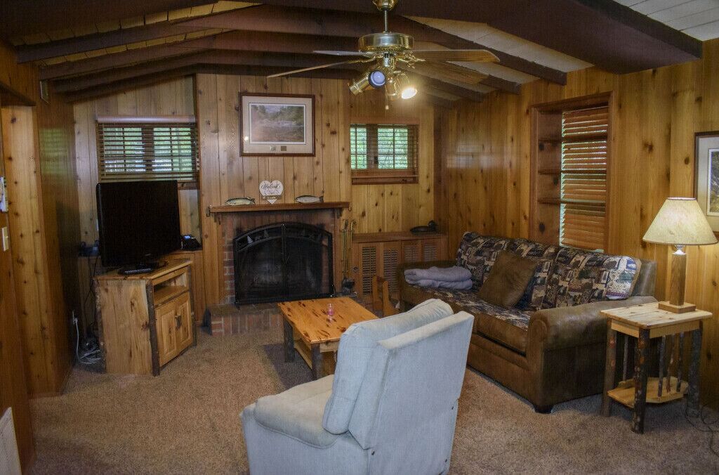 A cozy cabin interior with a fireplace, a television, a sofa, and a ceiling fan.