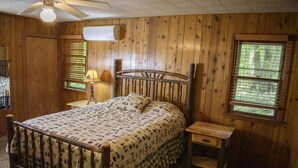 Une pièce aux murs lambrissés, avec un lit, une table de chevet, une lampe et une fenêtre.