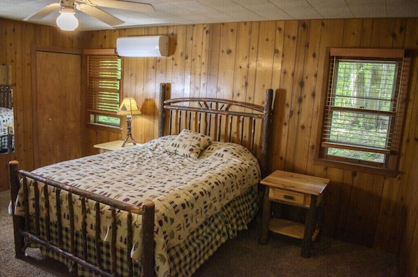 Ein Zimmer mit Holzwänden, einem Bett, einem Nachttisch, einer Lampe und einem Fenster.