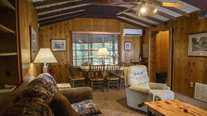 Une pièce chaleureuse avec des murs en bois, un ventilateur de plafond, une table à manger avec des chaises, un canapé et un fauteuil confortable.