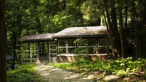 Un chalet rustique doté de grandes fenêtres et d’une terrasse en bois, entouré d’une forêt dense.