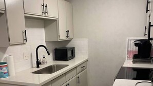 A kitchen with white cabinets, a stainless steel sink, a microwave, and a coffee machine. - NOLA Vibe/Oversized 1 bedroom/Entire unit (Kansas City)