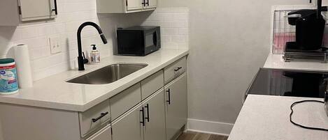 A kitchen with white cabinets, a stainless steel sink, a microwave, and a coffee machine.