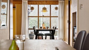A dining area with a wooden table, chairs, and a view through large windows. - 5 bedroom amazing home in Herning (Herning)