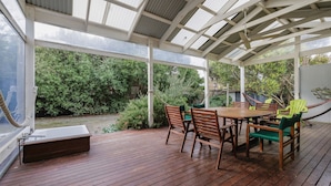 A covered patio with a wooden deck, a table with chairs, and a hammock. - Purple Goose at Red Rocks (Cowes)