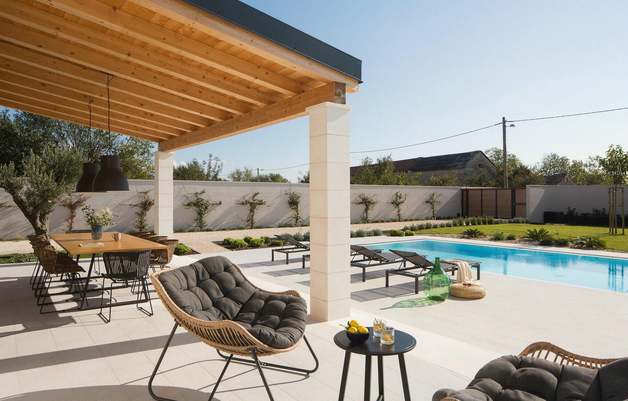 Un espace extérieur aménagé avec une terrasse, une piscine, une pergola en bois et des coins salon.