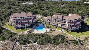 Un resort con dos edificios grandes, una piscina central y un paisaje natural circundante.