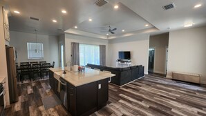 A modern kitchen with a central island, dining area with chairs, a sofa, and a TV. -  New Home only minutes away from beautiful sandy beaches (Port Charlotte)