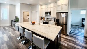 A modern kitchen with white cabinets, stainless steel appliances, a marble island with bar stools, and a wooden floor. -  New Home only minutes away from beautiful sandy beaches (Port Charlotte)