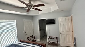 A bedroom with a bed, ceiling fan, TV, and a bathroom visible through an open door.