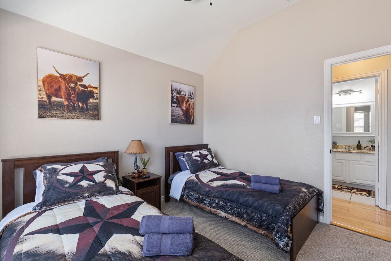 A bedroom with two beds, a nightstand, a lamp, and two framed pictures on the wall.