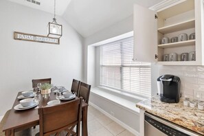 A kitchen with a dining table set for four, a coffee maker, and a window with blinds.