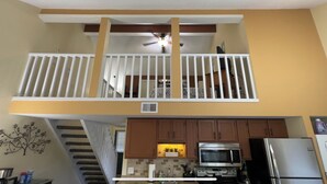 A kitchen with a built-in microwave, oven, and refrigerator. There is a wooden staircase leading to an upper level with a white railing.