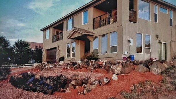 A two-story house with a balcony, large windows, and a stone foundation.