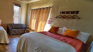 A hotel room with a large bed, a sofa, a small table, and a window with blinds.