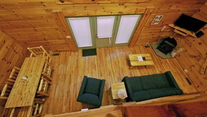 L’intérieur d’un chalet en bois comprend une table à manger, deux canapés verts, un téléviseur et une cheminée.