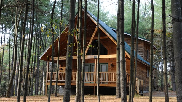 Une cabane en rondins dotée d’un balcon, entourée de grands arbres.
