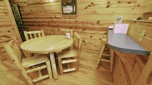 A wooden cabin interior with a round wooden table and chairs, a small stool, and a counter with a menu. - 1 Bedroom 1 Bath Cabin with hot tub (Beaver, WV) (Beaver)