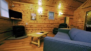 A cozy cabin interior with a wooden floor, a sofa, a table, a television, and a fireplace. - 1 Bedroom 1 Bath Cabin with hot tub (Beaver, WV) (Beaver)