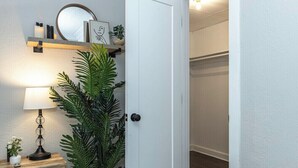 Un couloir avec une porte blanche, une table de chevet en bois avec une lampe et une plante en pot.