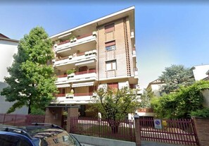Un edificio residencial de varios pisos con balcones, un acceso con portón y un árbol en la parte delantera.