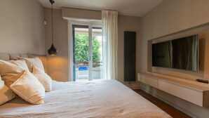 A bedroom with a large bed, a TV mounted on the wall, and a sliding glass door leading to an outdoor area. - Beautiful 2-bed Apartment in Torino (Turin)