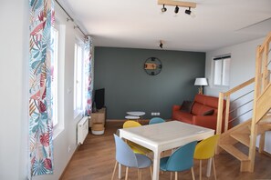 Un salon chaleureux avec une table à manger, des chaises colorées, un canapé et un escalier.