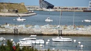 A marina with several boats docked, a stone wall, and a building with a unique sloped roof in the background. - Appartement Avec Magnifique vue sur Port Situé Entre la Plage et le Centre Ville (Calais)