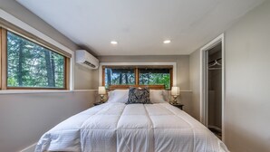 Een slaapkamer met een groot bed, twee nachtkastjes met lampen, een raam met uitzicht op bomen, en een airconditioning.