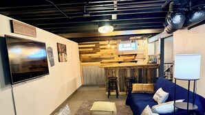Quarto com televisão, sofá, área de bar com banquetas e quadro branco.
