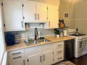 A kitchen with white cabinets, a stainless steel sink, a coffee maker, a toaster, and a stove.
