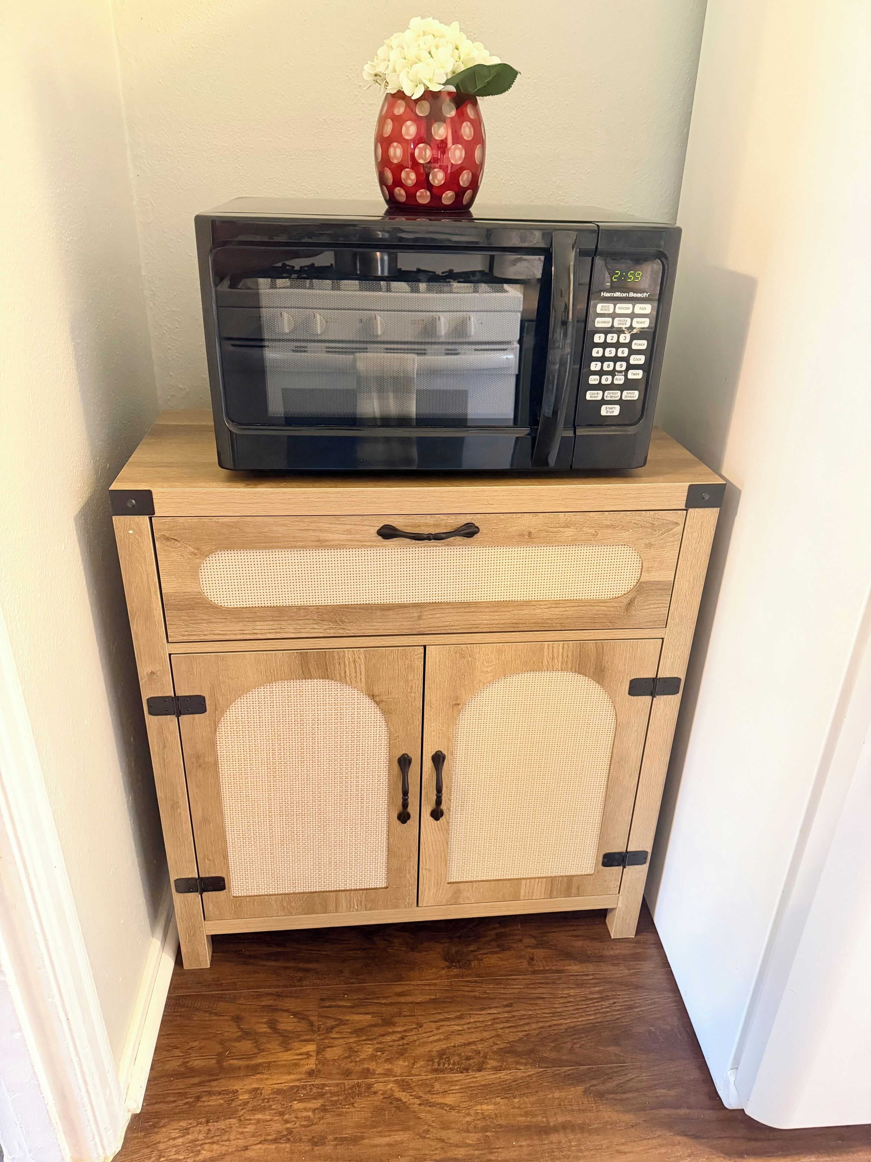 Un forno a microonde su un mobile in legno con ante intrecciate.