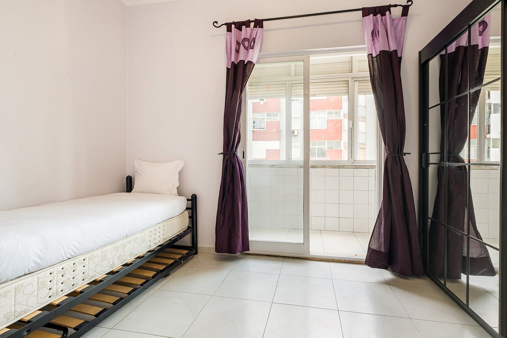 Un dormitorio con una cama, un ventanal corredero a un balcón y cortinas moradas.