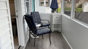 Varanda coberta com cadeira, mesa, um guarda-sol azul e vista para uma área residencial.