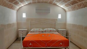 Ein Schlafzimmer mit Ziegeldecke, einem Bett mit orangefarbener Bettdecke, zwei Nachttischen und einer Wand-Klimaanlage.