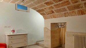 Ein Zimmer mit weißem Schminktisch, einem roten Sessel, einer Heizung und einer Ziegeldecken.