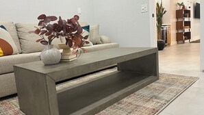 Un salon moderne avec une table basse grise, un canapé beige et un tapis à motifs.