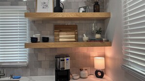 Une cuisine équipée d’une machine à café, d’une lampe et d’étagères où sont rangés des livres et des objets décoratifs.