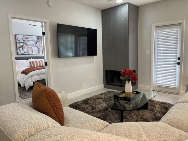 A modern living room with a sofa, a coffee table, a fireplace, and a TV mounted on the wall.