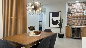 Un espace repas moderne avec une table en bois, des chaises à revêtement gris, un luminaire décoratif et un mur arrière orné d’un motif.