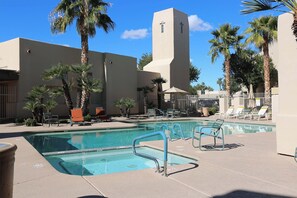 A pool area with lounge chairs, palm trees, and a building with a cross on its tower.