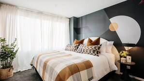 A modern bedroom with a large bed, a geometric wall mural, and a bedside table with a lamp and flowers. - Midnight Moonshine Loft ITAS (LAUNCESTON)