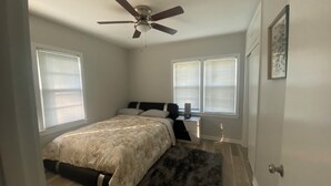 Ein Schlafzimmer mit Bett, Deckenventilator und zwei Fenstern mit Jalousien.