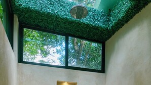 A modern bathroom with a freestanding bathtub, recessed lighting, and a view of greenery through a window.