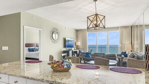A modern kitchen with granite countertops, a dining area with wicker furniture, and a large window offering a view of the ocean. - Majestic Sun A1206*12th-Top Floor*Gulf View*6 Beds*Heated Pool/Hot Tubs*Gym (Miramar Beach)