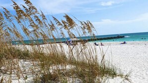 A beach with sand, seaweed, and a pier in the background. - Free Heated Pool Oasis: Coastal Bungalow Near Town & Beach (Bradenton)