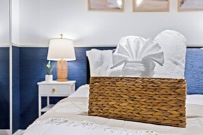 A neatly made bed with a white comforter and a woven basket filled with white towels.